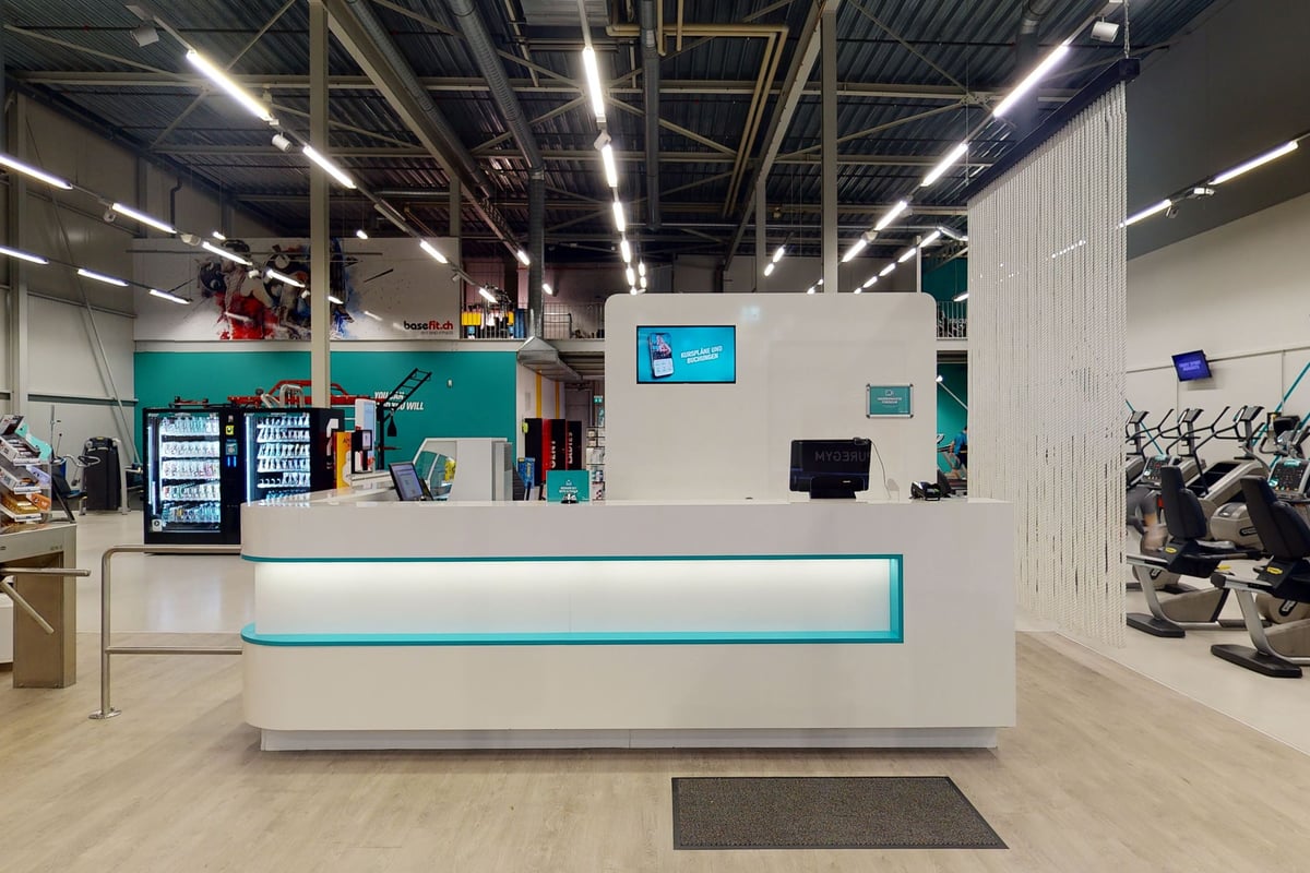 PureGym Oftringen: Gym reception with service counter, vending machines, seating area, and equipment racks visible.