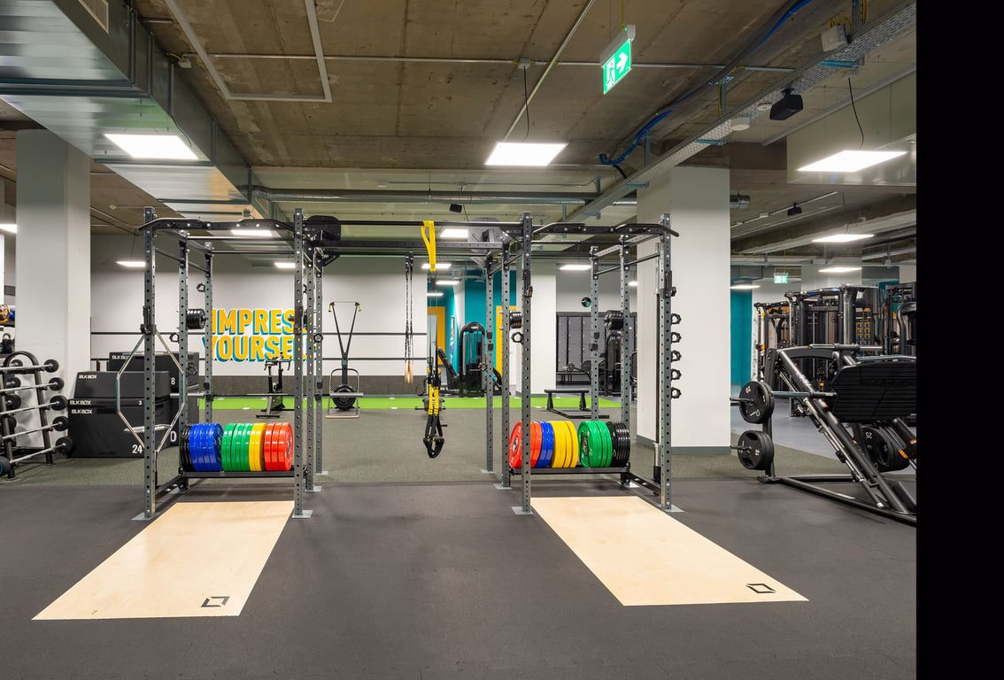 PureGym La Chaux-de-Fonds: Gewichtheberständer, Teller in verschiedenen Farben, gummierter Boden und verspiegelte Wände.