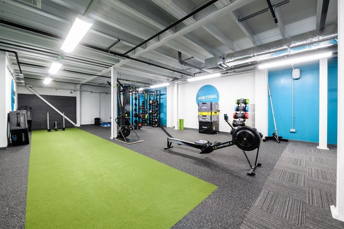 PureGym Glasgow Silverburn: Weight racks, kettlebells, rowing machine, turf area, with exposed ceiling ducts and pipes.
