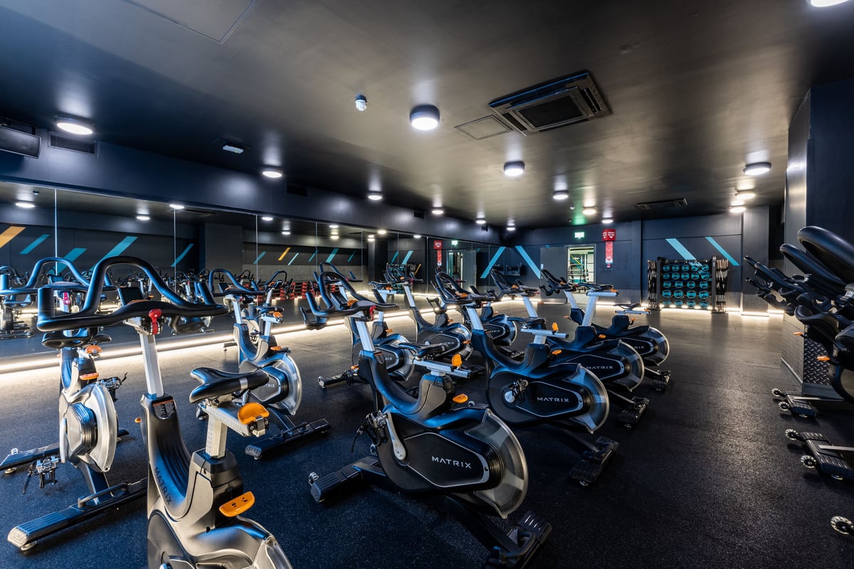 PureGym London Edgware: Rows of stationary bikes and treadmills in a dimly lit exercise studio.