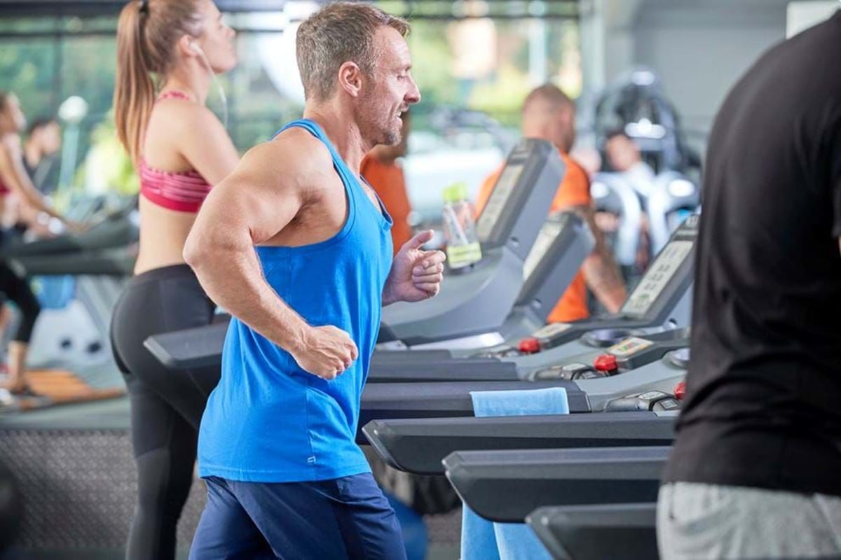 People running on treadmills in a gym with large windows in the background