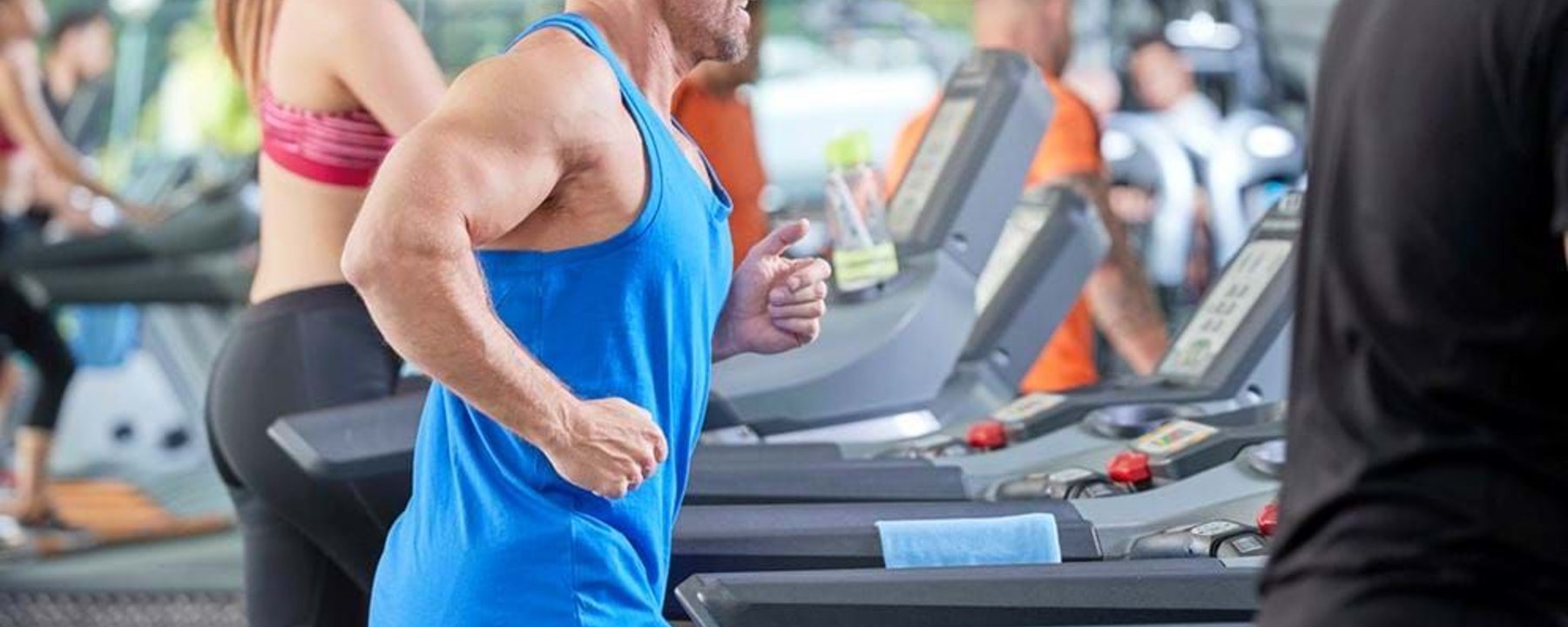 People running on treadmills in a gym with large windows in the background