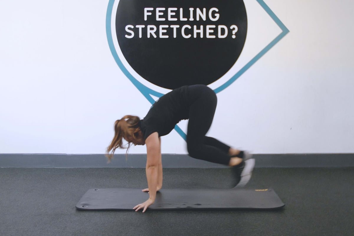 Woman in black workout clothes doing mountain climber exercise on mat indoors
