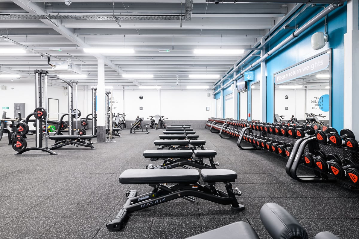 PureGym Aberdeen Wellington Circle: Rows of benches, weight racks, free weights, and rubberized floors in a gym facility.