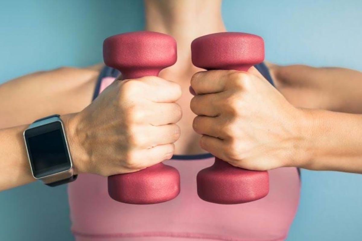 Person in pink sports bra holding two pink dumbbells with a smartwatch on wrist