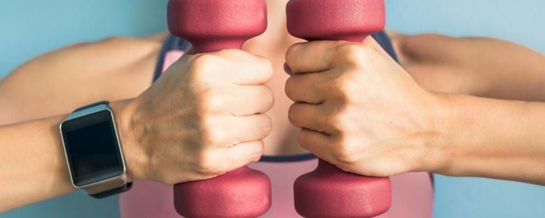 Person in pink sports bra holding two pink dumbbells with a smartwatch on wrist