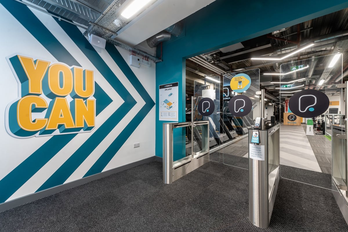 PureGym London Monument: Gym entrance with motivational "You Can" signage, turnstiles, and exercise machines visible.