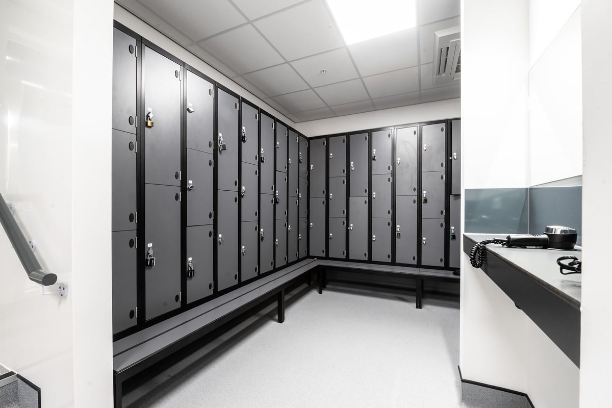 PureGym London Woolwich: Rows of metal lockers, benches in a changing room setting.
