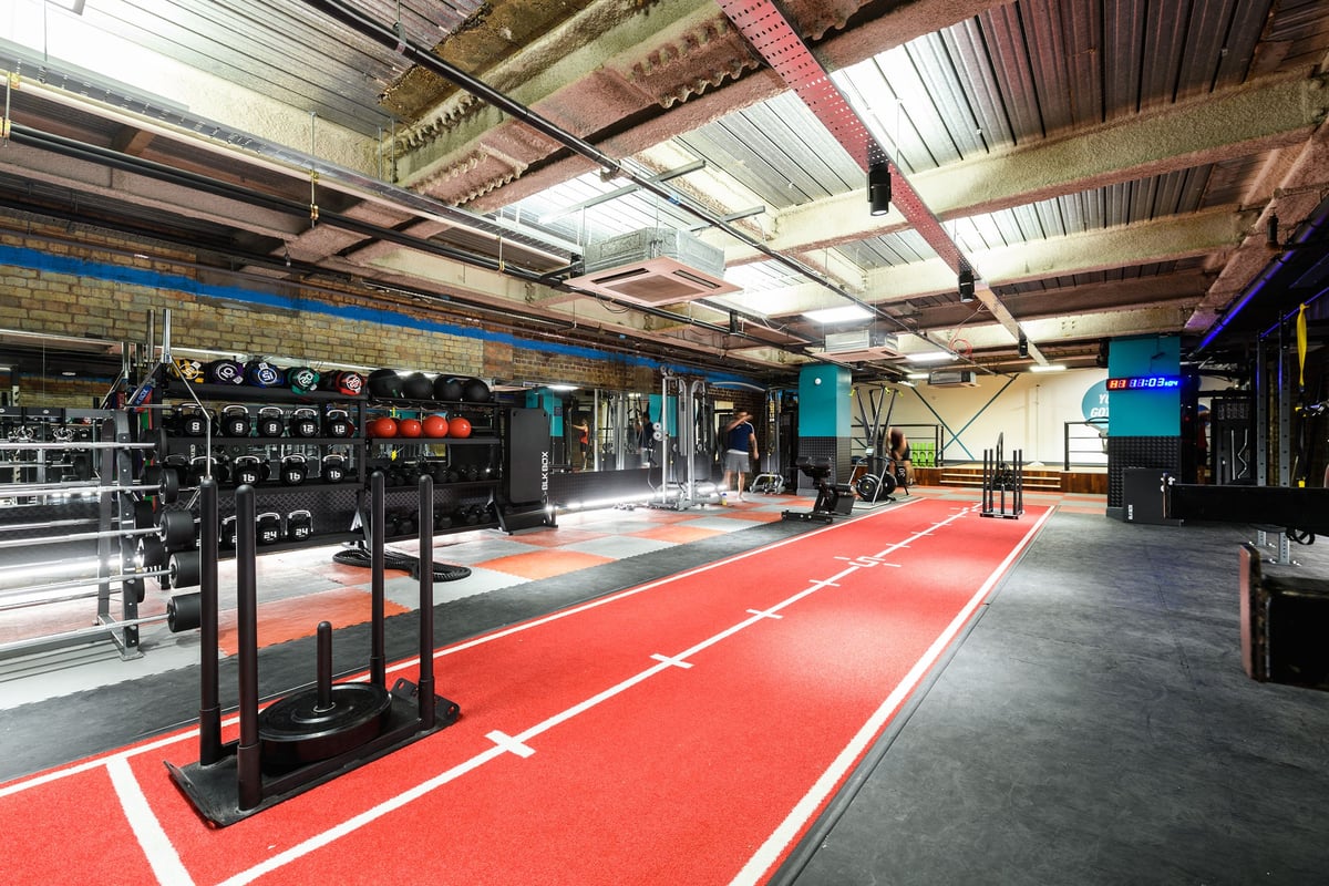 PureGym London Tower Hill: Weightlifting area with barbell racks, weight plates, squat stands, rubberized flooring.
