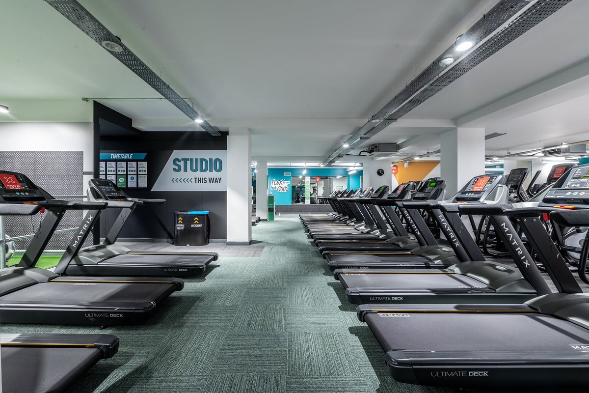PureGym London Twickenham: Rows of treadmills, studio signage, and ventilation ducts in a modern fitness centre.