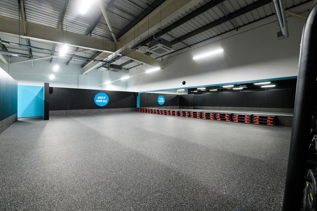 PureGym Cardiff Bay: Rows of speed bags, rubberized flooring, and mirrored walls in a fitness studio.