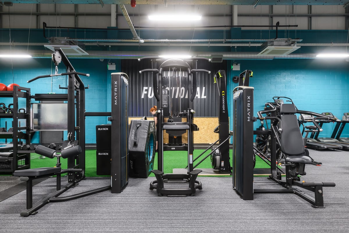PureGym Buckingham: Strength machines, cable stations, benches, and rubberized flooring in a dimly lit gym.