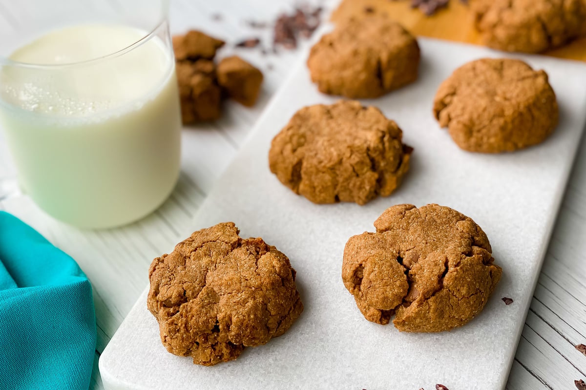 Freshly baked protein cookies arranged on white parchment beside a glass of milk