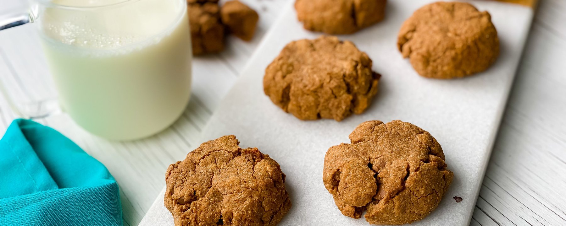 Freshly baked protein cookies arranged on white parchment beside a glass of milk
