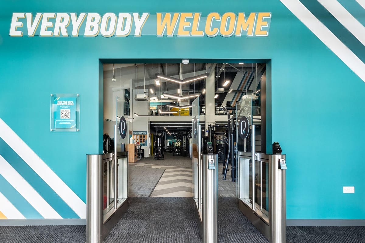 PureGym Kettering: Gym entrance with turnstiles, "Everybody Welcome" signage, tiled flooring.