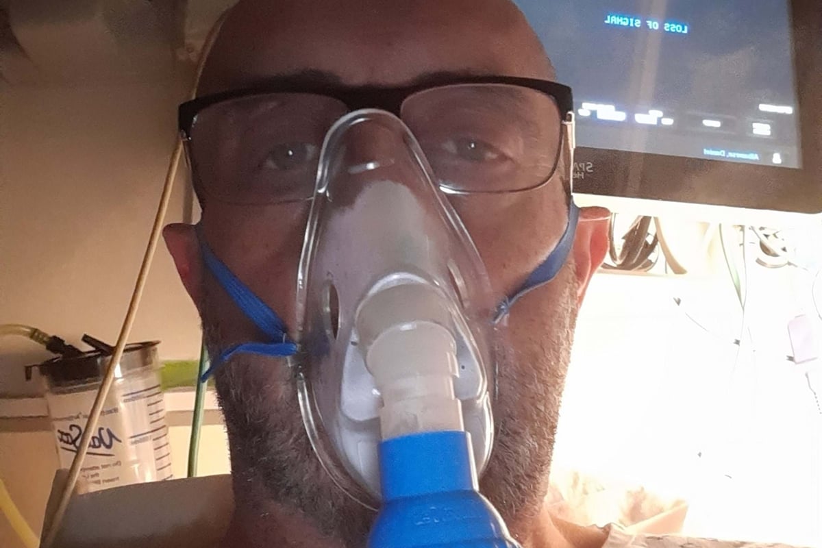 Man wearing oxygen mask and hospital gown with heart monitor in background