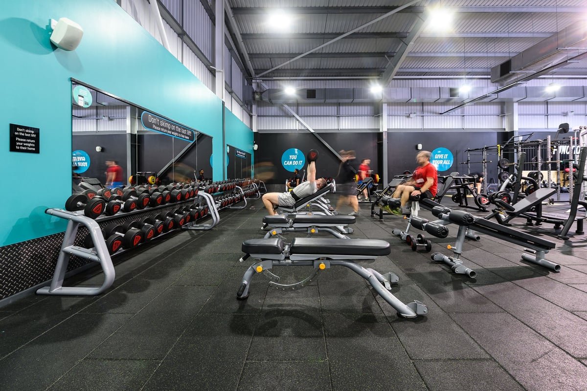 PureGym Widnes: Extensive weight training area with rows of free weights, benches, and resistance machines.