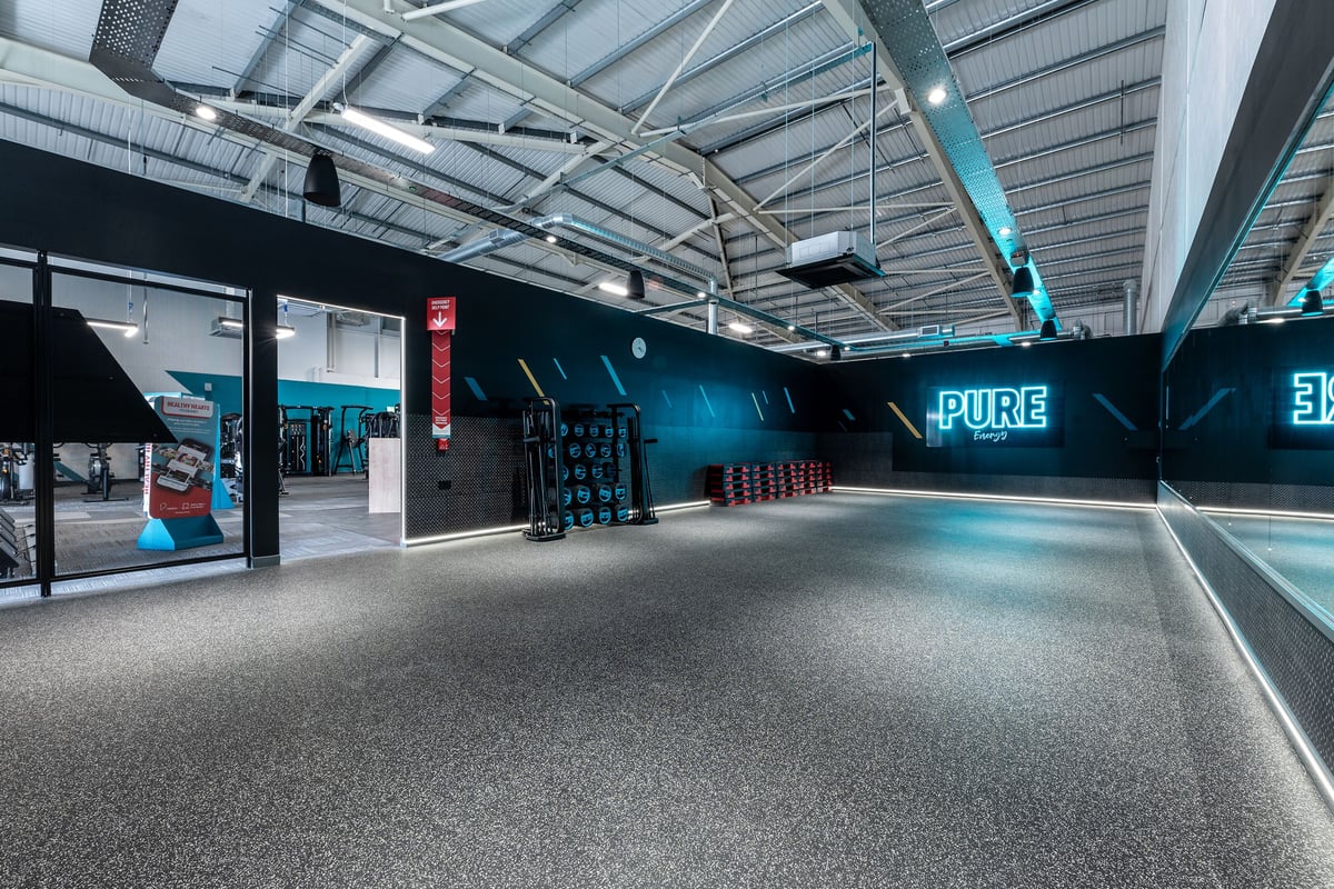 PureGym Durham City Retail Park: Weights rack, punching bags, rubberized flooring in a dimly lit fitness studio.