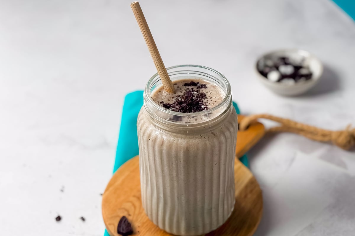 Smoothie in ridged glass jar topped with biscuit crumbles on wooden coaster