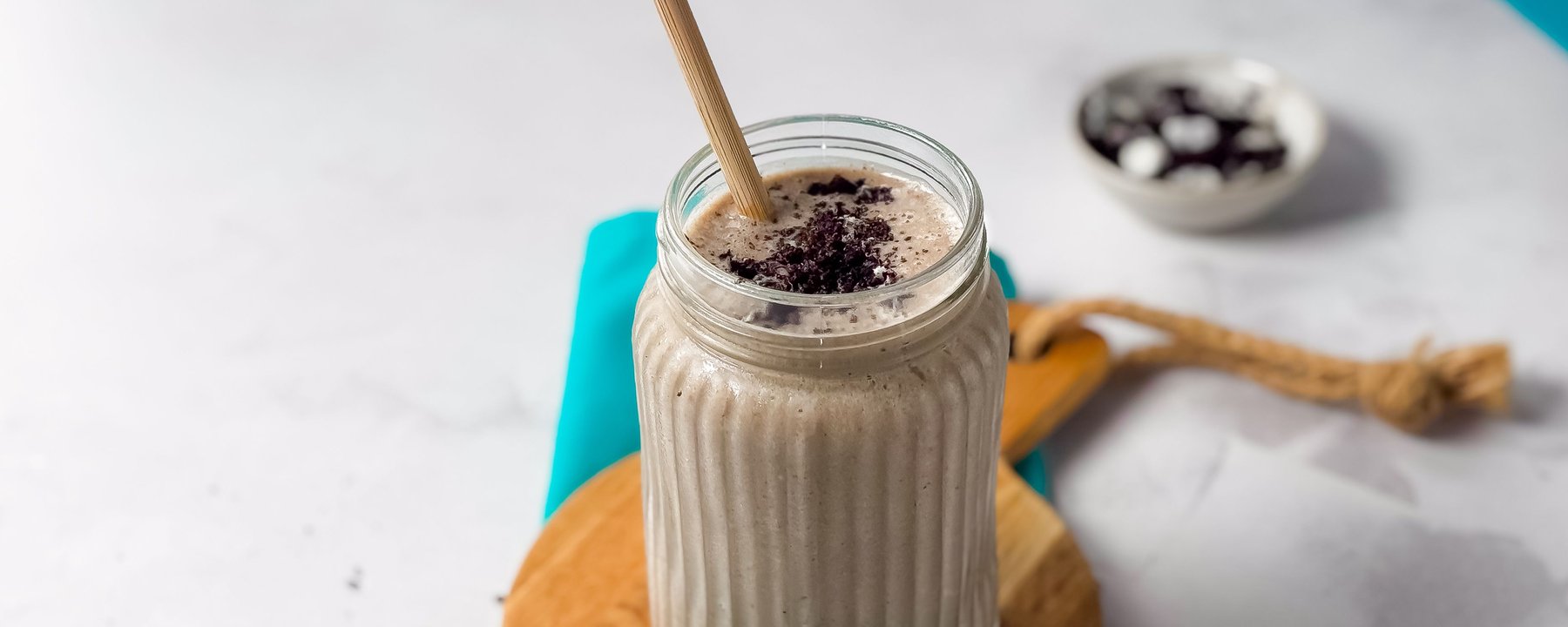 Smoothie in ridged glass jar topped with biscuit crumbles on wooden coaster