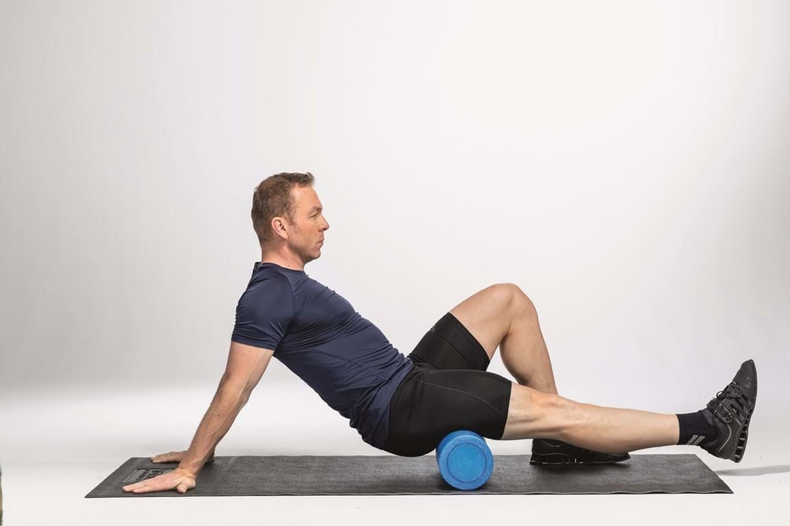 Man using a foam roller on his calf while sitting on a mat against a white background