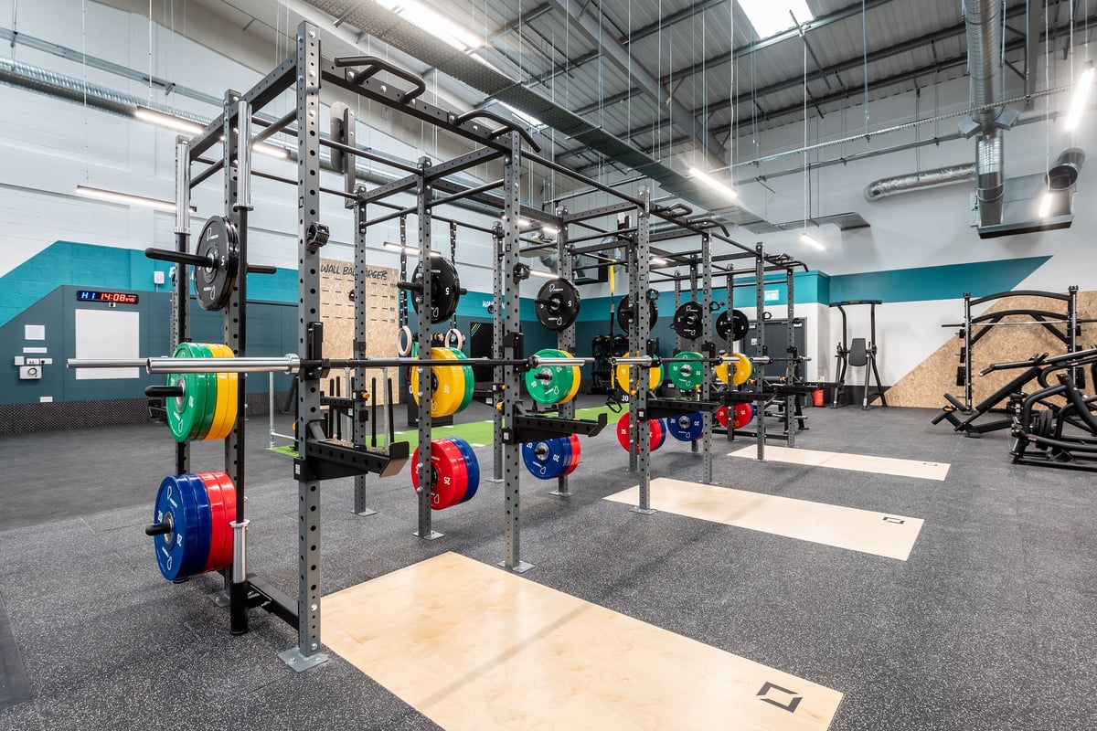 PureGym Thamesmead: Strength racks, heavy weights in vibrant colours, rubber flooring in an industrial gym setting.