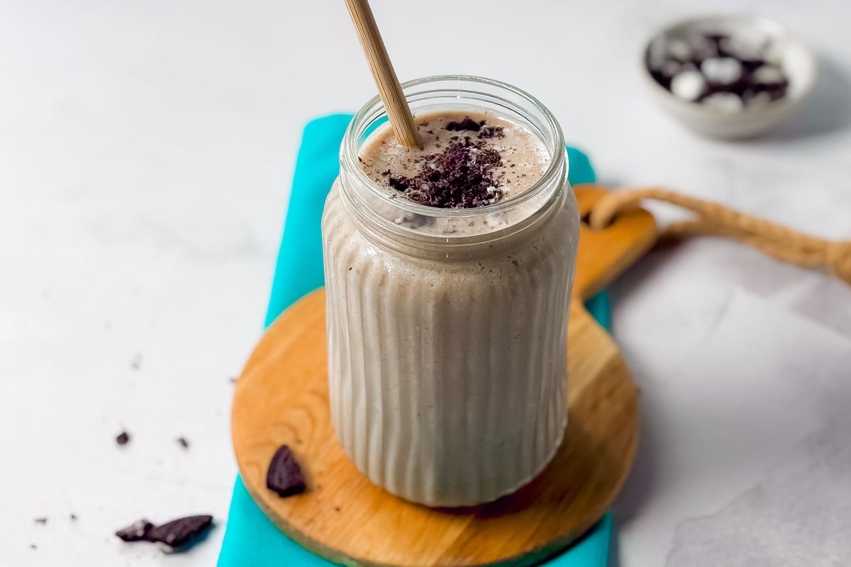 Chocolate milkshake in a glass jar with a straw on a wooden board and blue cloth