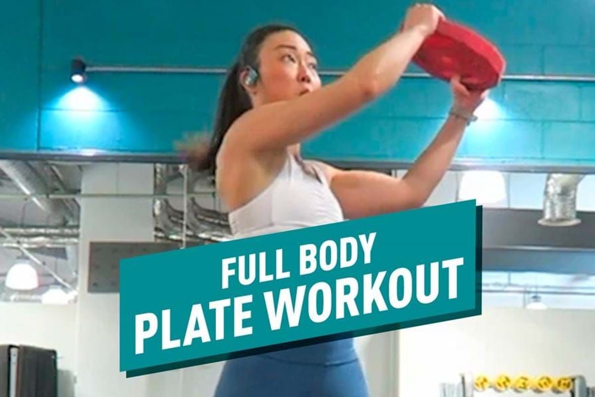 Woman in gym lifting red weight plate during workout session