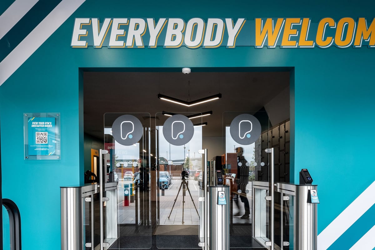 PureGym Selby: Gym entrance area with turnstiles and self-service kiosks, featuring an "Everybody Welcome" sign.