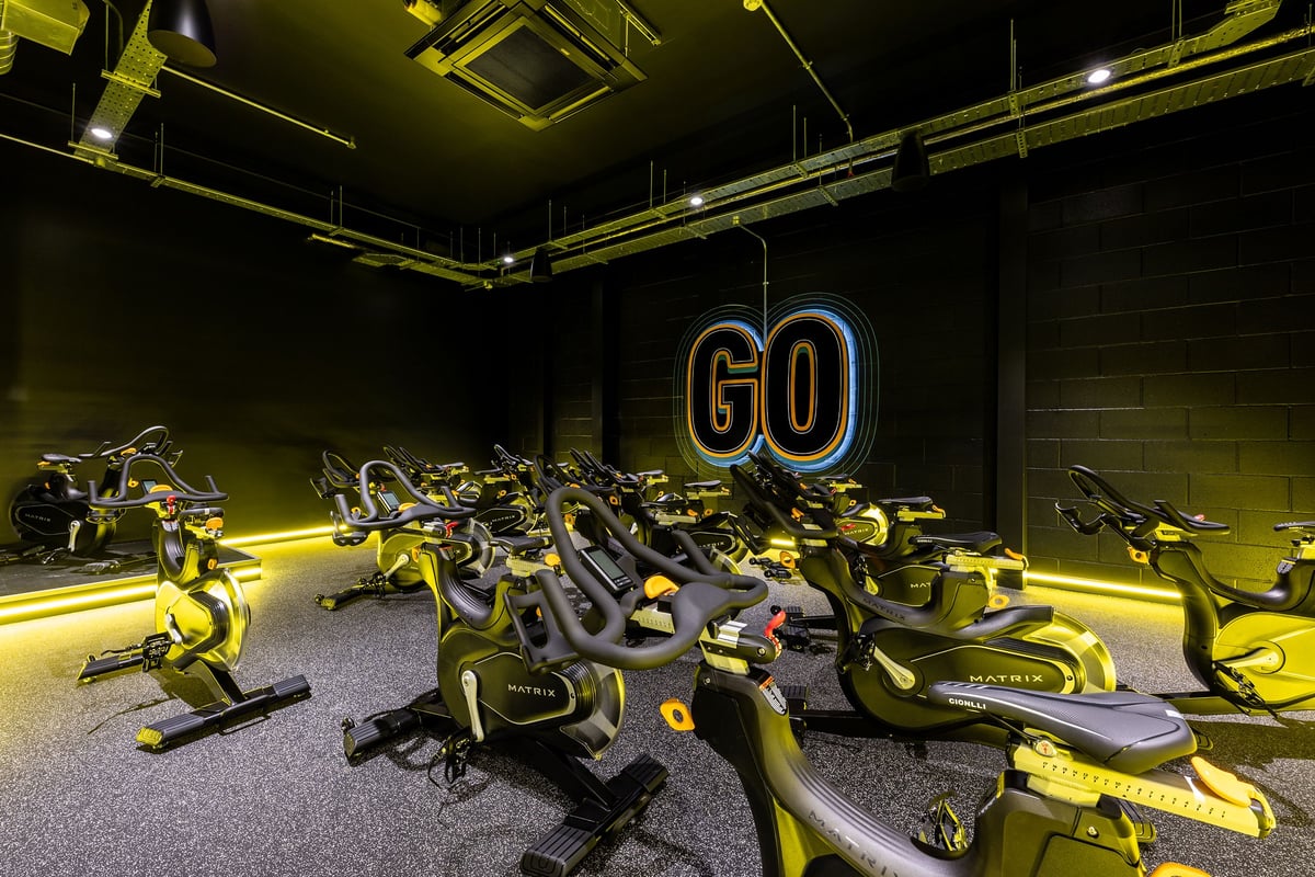 PureGym Dagenham: Rows of stationary cycles, illuminated by neon lighting in a darkened fitness studio.