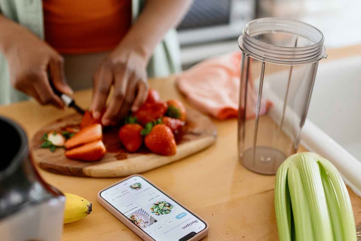 Person bereitet frisches Gemüse in der Küche zu, Smartphone mit Rezept auf der Arbeitsplat