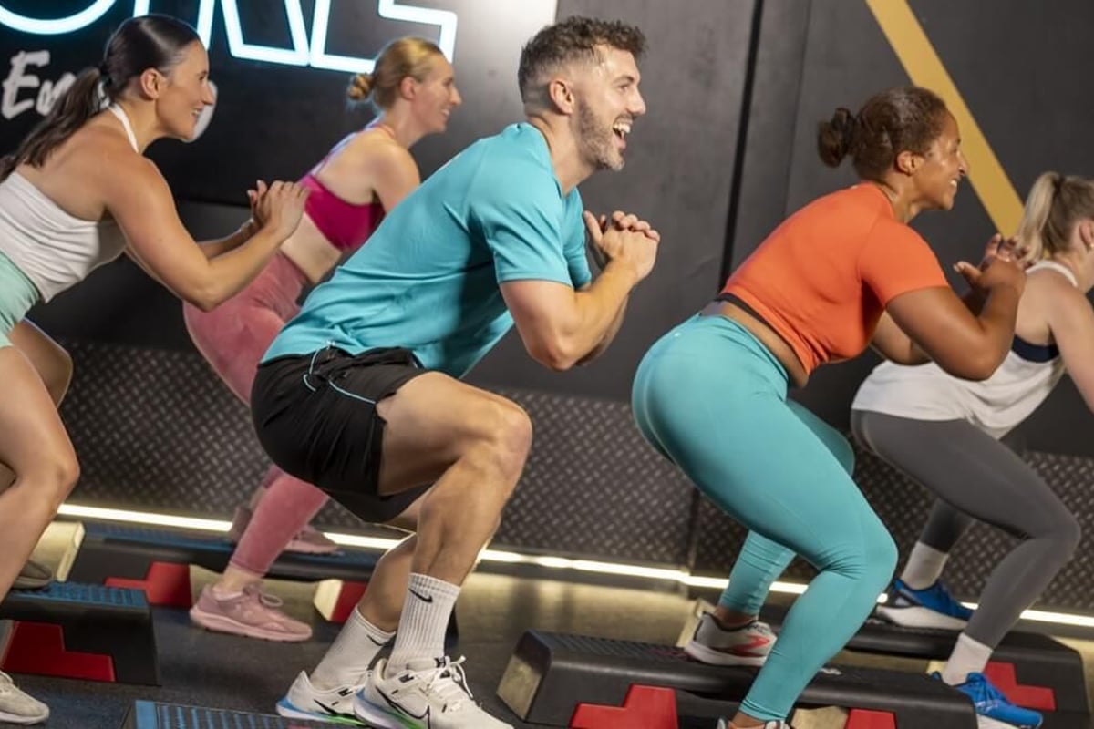 Group of five people performing step-ups on aerobic platforms in a fitness studio