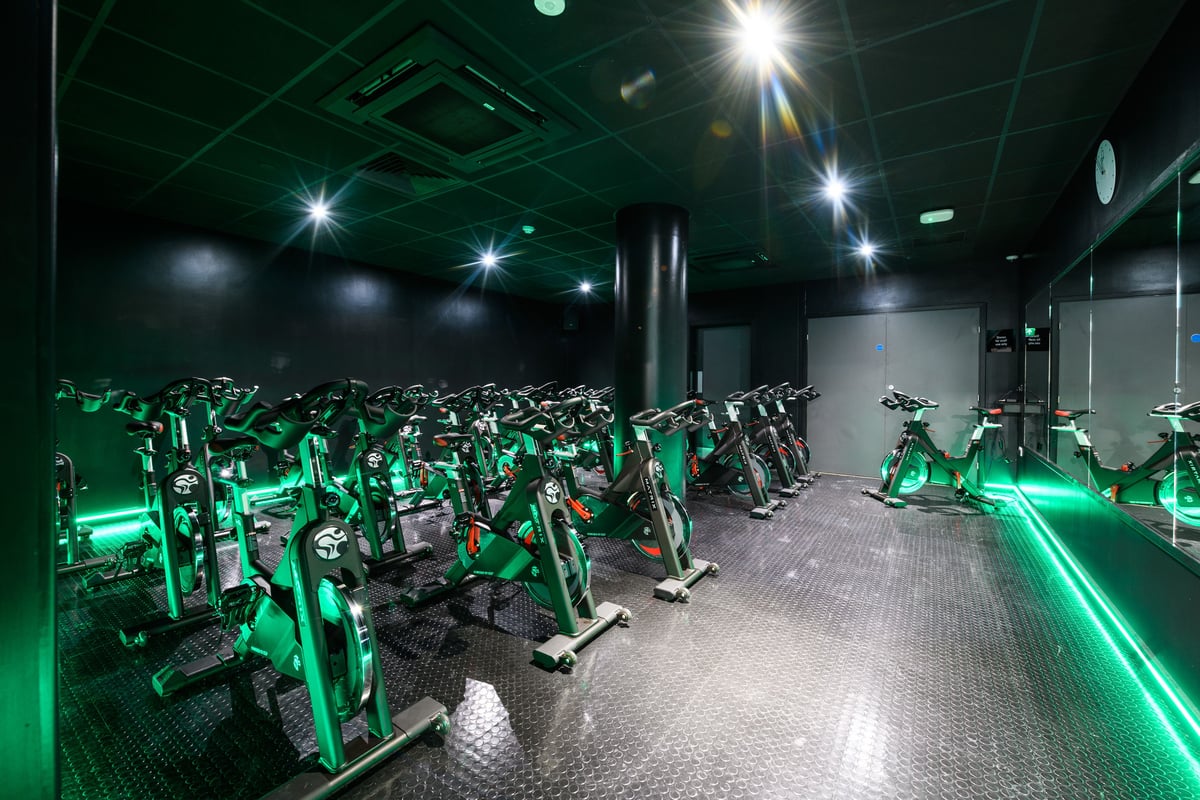 PureGym London East India Dock: Rows of stationary bikes illuminated with neon green lighting.
