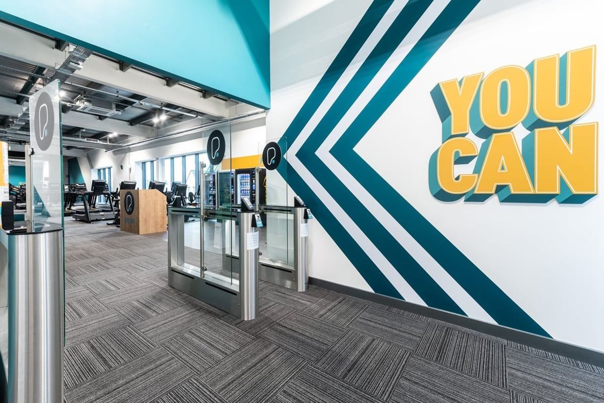 PureGym Bicester: Turnstiles, closed kiosks, "You Can" motivational signage in a modern gym setting.