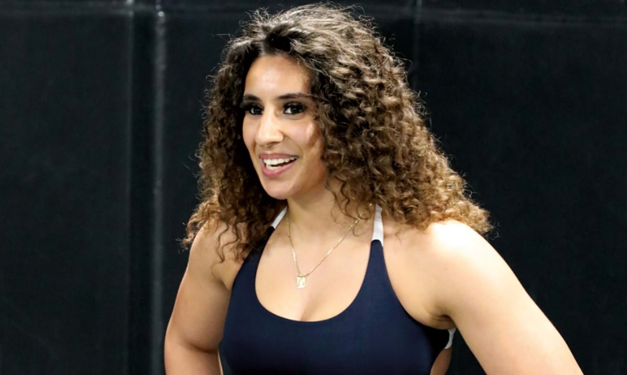 Smiling woman with curly hair wearing a navy blue sports top against a dark background