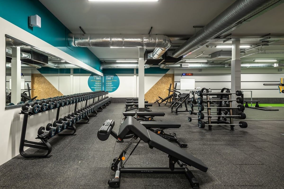 PureGym Llantrisant: Rows of benches, weight racks, dumbbells, and rubberized flooring in a gym studio.