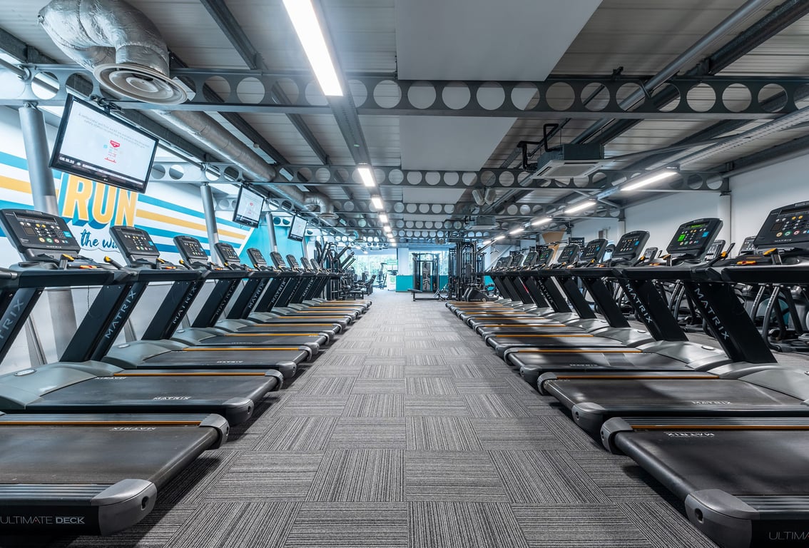 PureGym London Finchley: Rows of treadmills with TV screens and ceiling mirrors in a brightly lit gym interior.