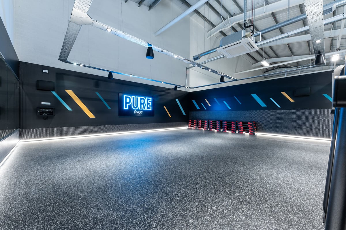 PureGym Byfleet: Indoor running track with neon lights, padded floor, and spectator seating.