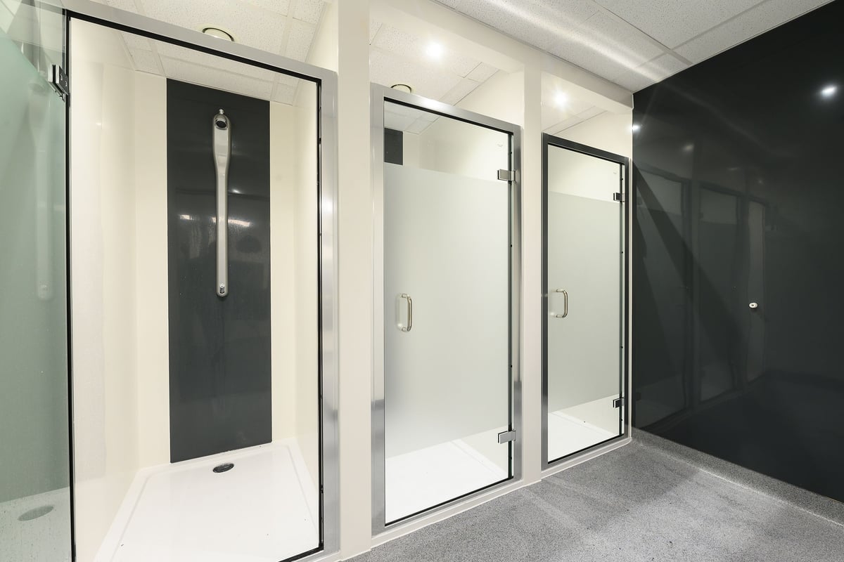 PureGym Bromsgrove Retail Park: Rows of shower cubicles with frosted glass doors and metal frames.