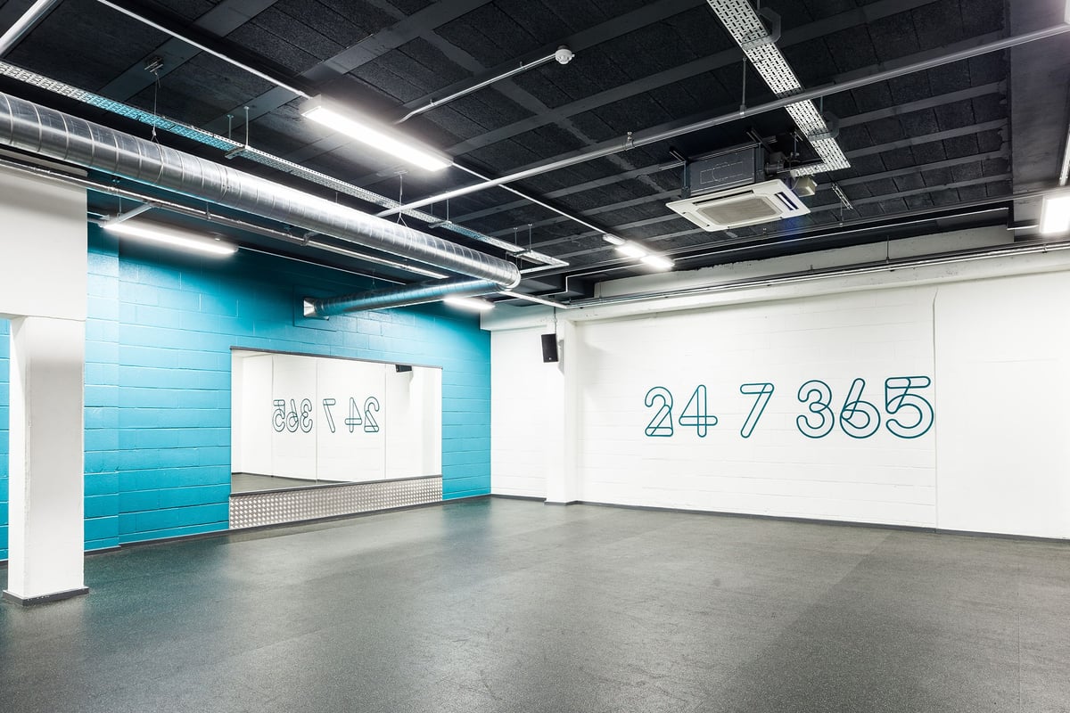 PureGym Altrincham: Gym studio with white and teal walls, rubberised floorin g, and 24 7 365 painted on the wall.