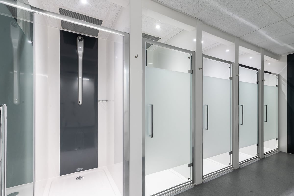PureGym Bath Victoria Park: Frosted glass shower cubicles with metallic frames and door handles in a changing room setting.