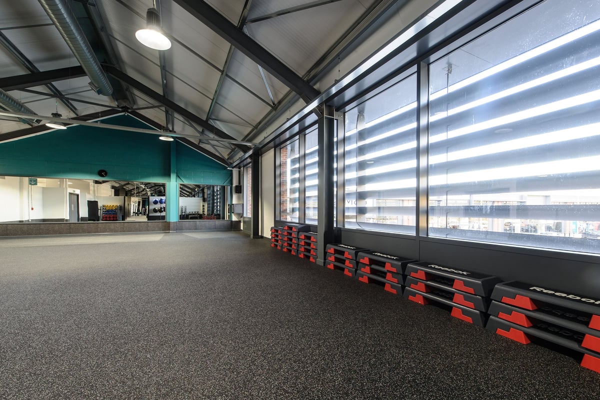 PureGym Leeds Kirkstall Bridge: Rows of red benches, rubberized flooring, glass walls in an indoor fitness studio.