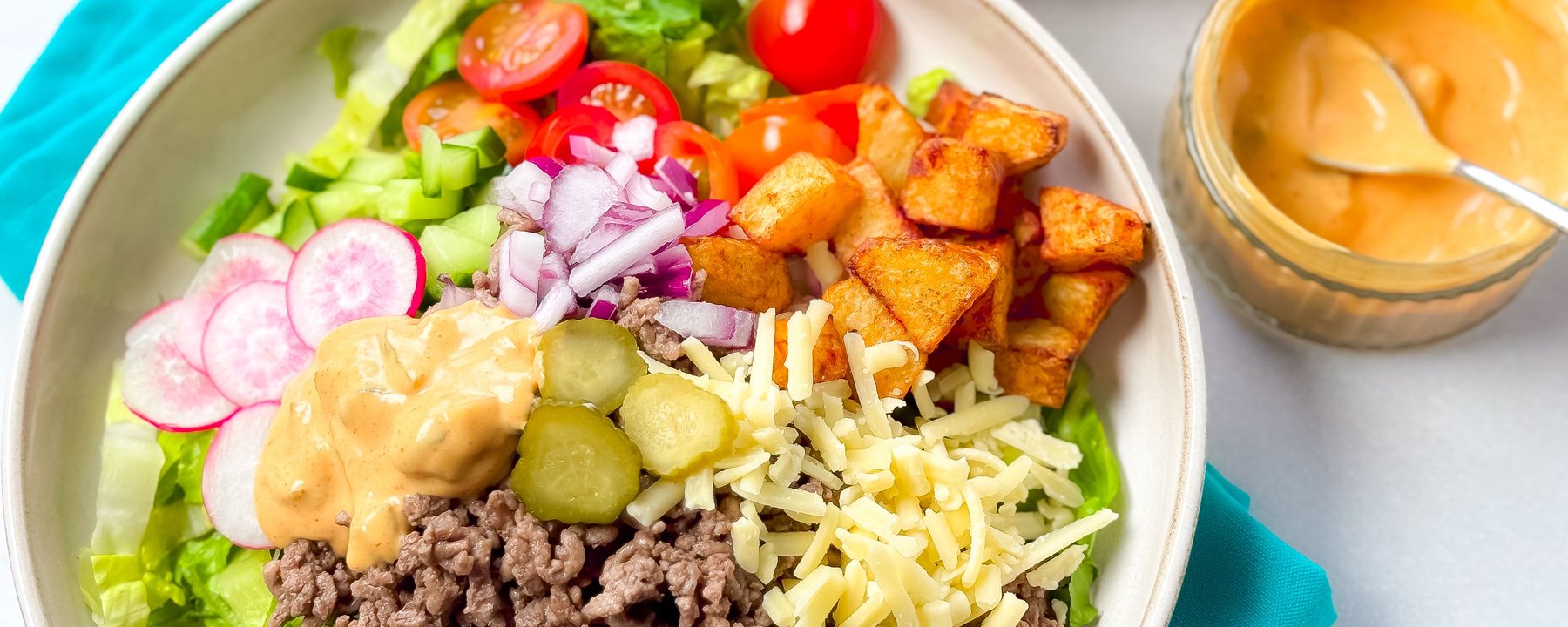 Bowl of salad with seasoned mince, lettuce, tomatoes, gherkins, cheese and dressing