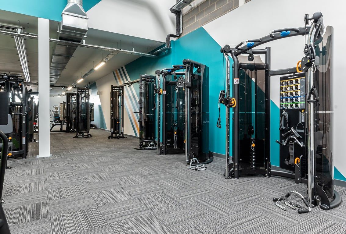 PureGym Sittingbourne: Rows of resistance machines, cable pulleys, and rubberized flooring in a teal-themed gym interior.