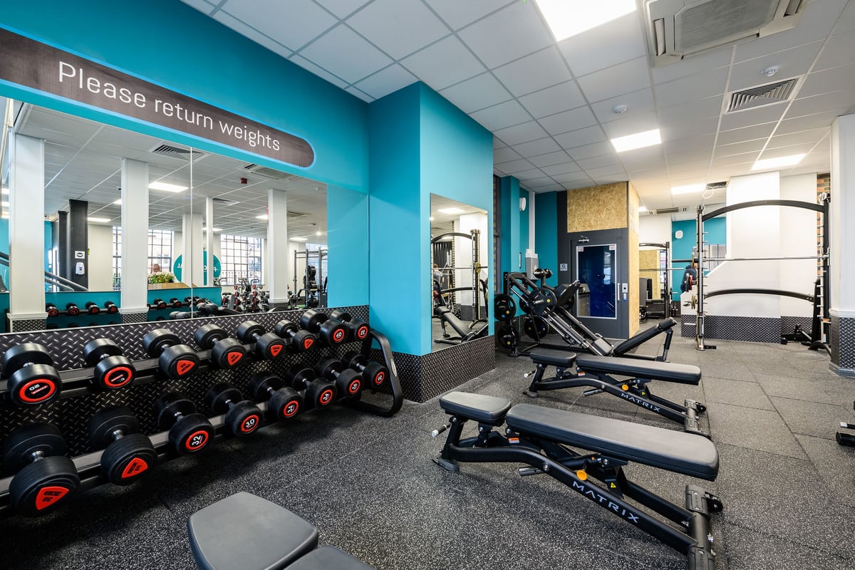 PureGym London Bow Wharf: Weight racks, benches, dumbbells, and teal accent walls in a gym setting.