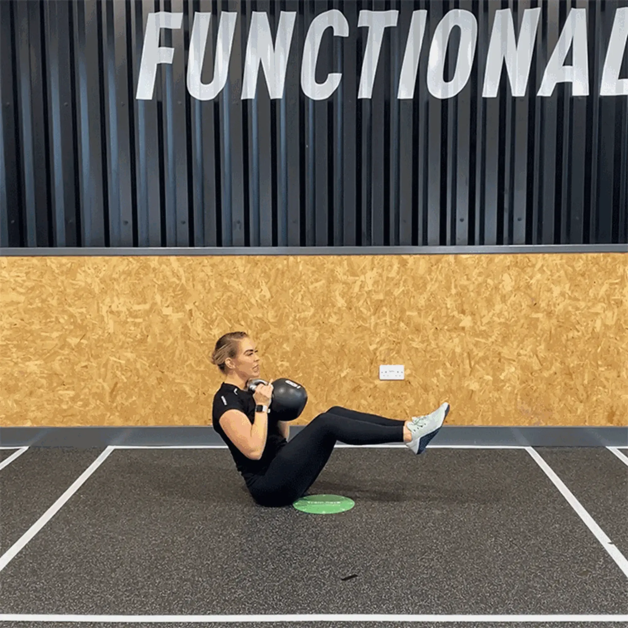 Woman in black workout clothes holding kettlebell while balancing on floor in gym