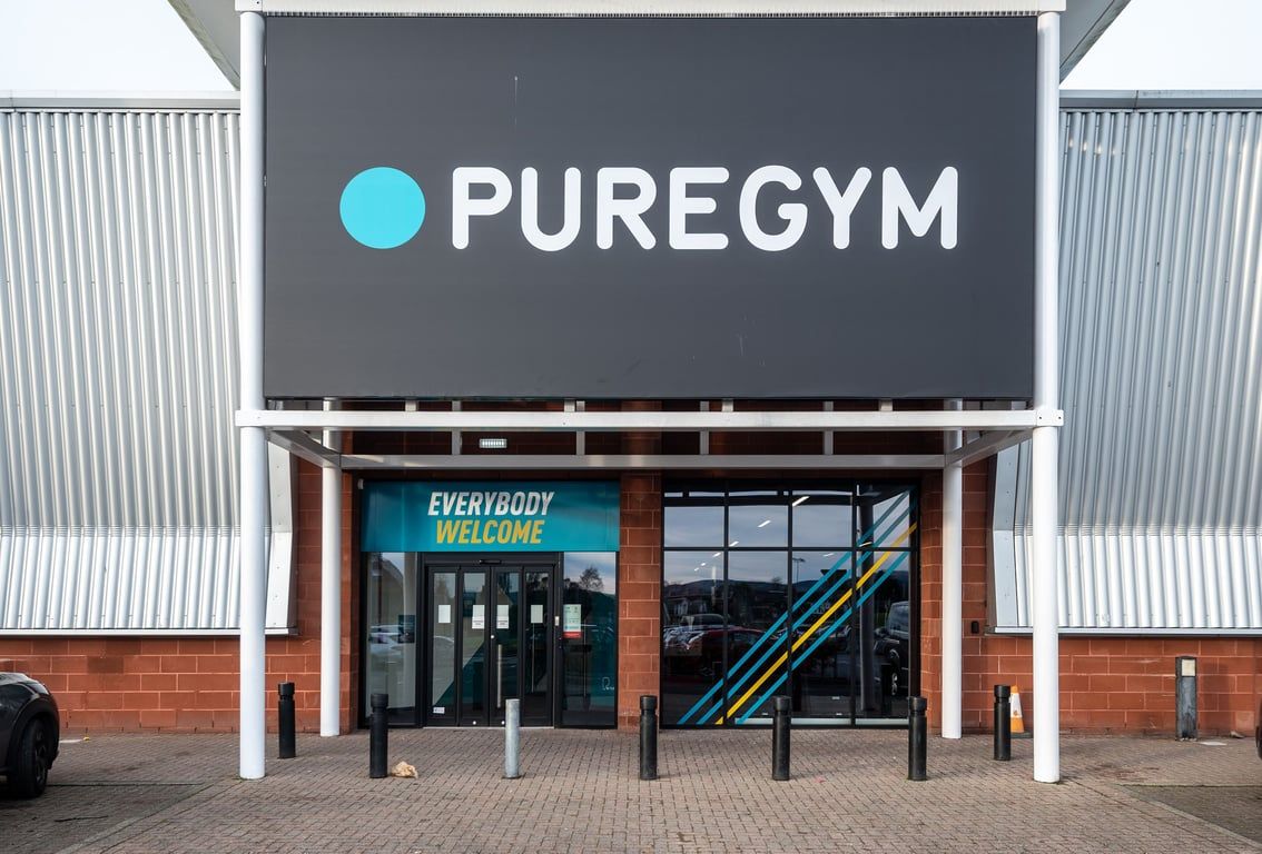PureGym Lanark: PureGym exterior with signage, entrance doors, and exercise equipment visible inside.