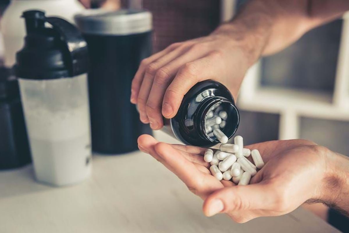 Hands pouring white capsules from a black bottle with shaker bottles in the background