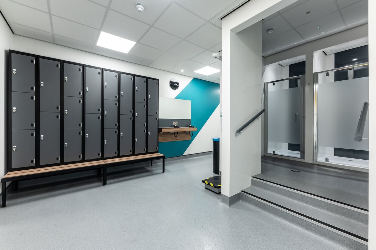 PureGym Durham City Retail Park: Locker room with rows of lockers, benches, and private shower cubicles.