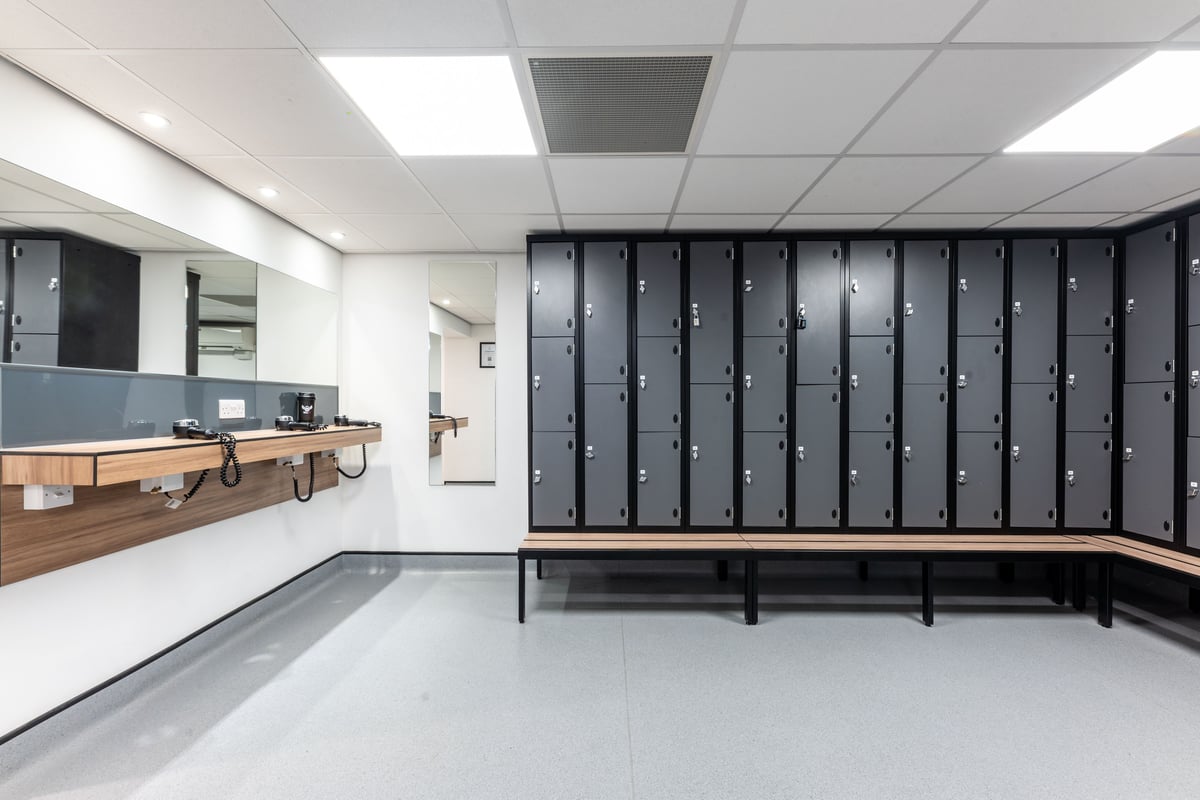 PureGym London Muswell Hill: Rows of lockers, wooden benches, and an attendant's counter in a changing room.